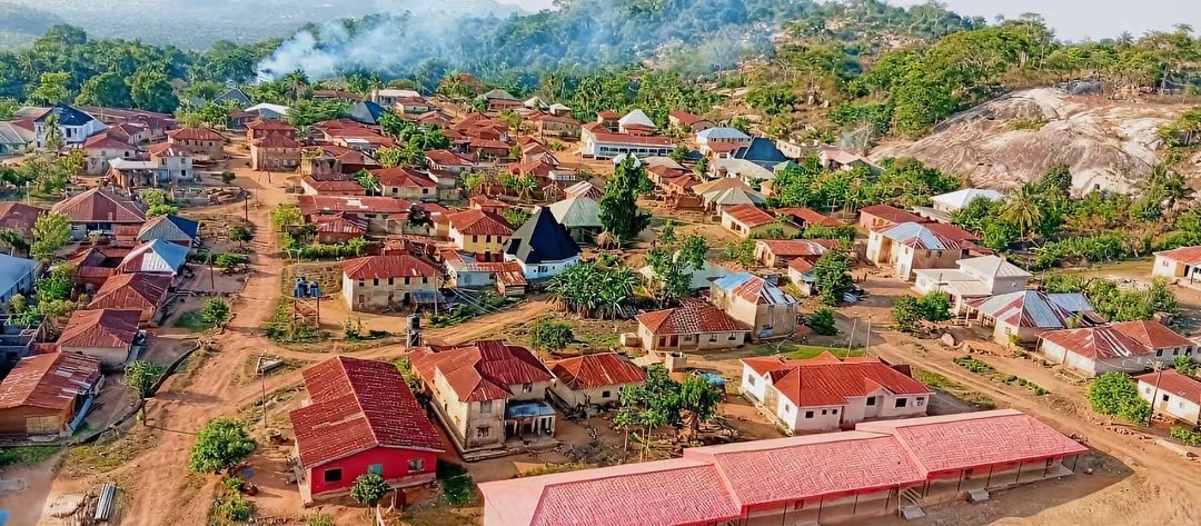 Aerial view over Makeke: rooftops and village roads spread among hills, forest and a rocky outcrop